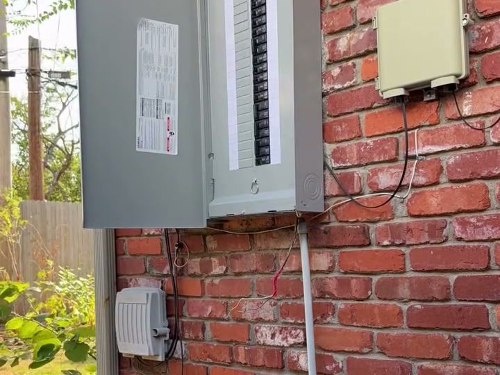 The new grey panel with its door open on the same brick wall, rows of new breakers inside.