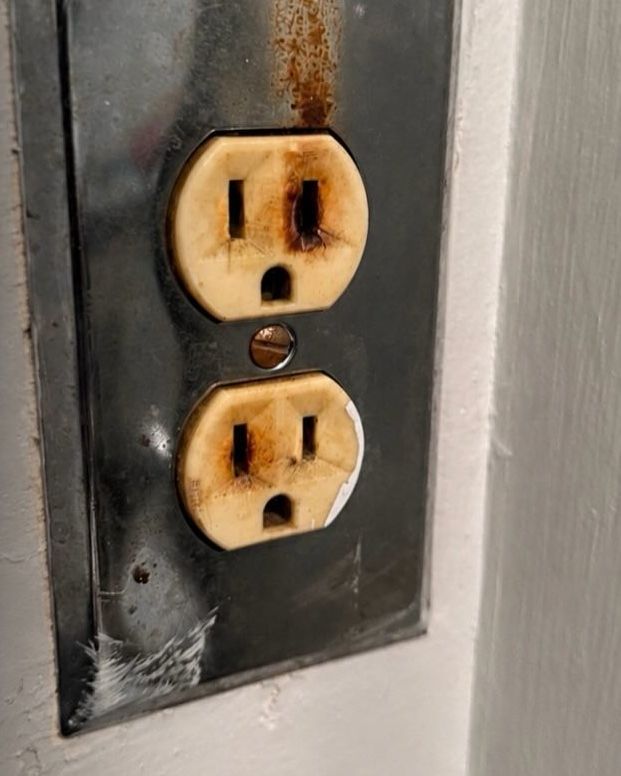 A scorched duplex receptacle in a blackened cover plate, burn marks around both outlets.
